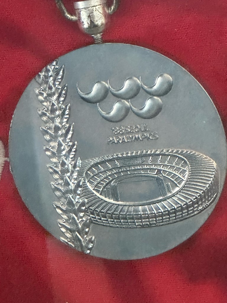 A silver medal from the 1988 Paralympic Games showing the 1988 logo above a stadium.