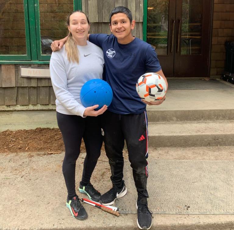 Eliana Mason, holding a goalball, and Ricky Castaneda, holding a blind soccer ball, pose together for a photo.