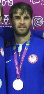 Matt is pictured wearing a silver medal around his neck and a blue United States Parapan Am Team jacket at the 2019 Parapan American Games in Lima, Peru.