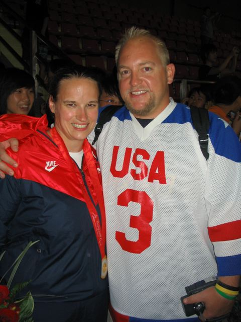 Jake Czechowski puts her arm around Lisa as they smile for the camera. Lisa is wearing her 2008 Paralympic gold medal around her neck and Jake is wearing a white USA jersey with the number 3 on the front.