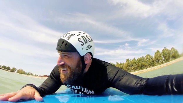 Snapshot of Joshua Loya smiling, paddling on a surfboard. 