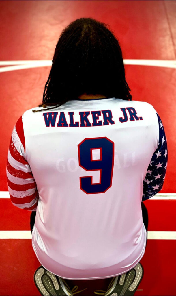 A photo of Sean Walker's back as he kneels on the floor. The back of his USA jersey has the name "Walker Jr." above the number 9.