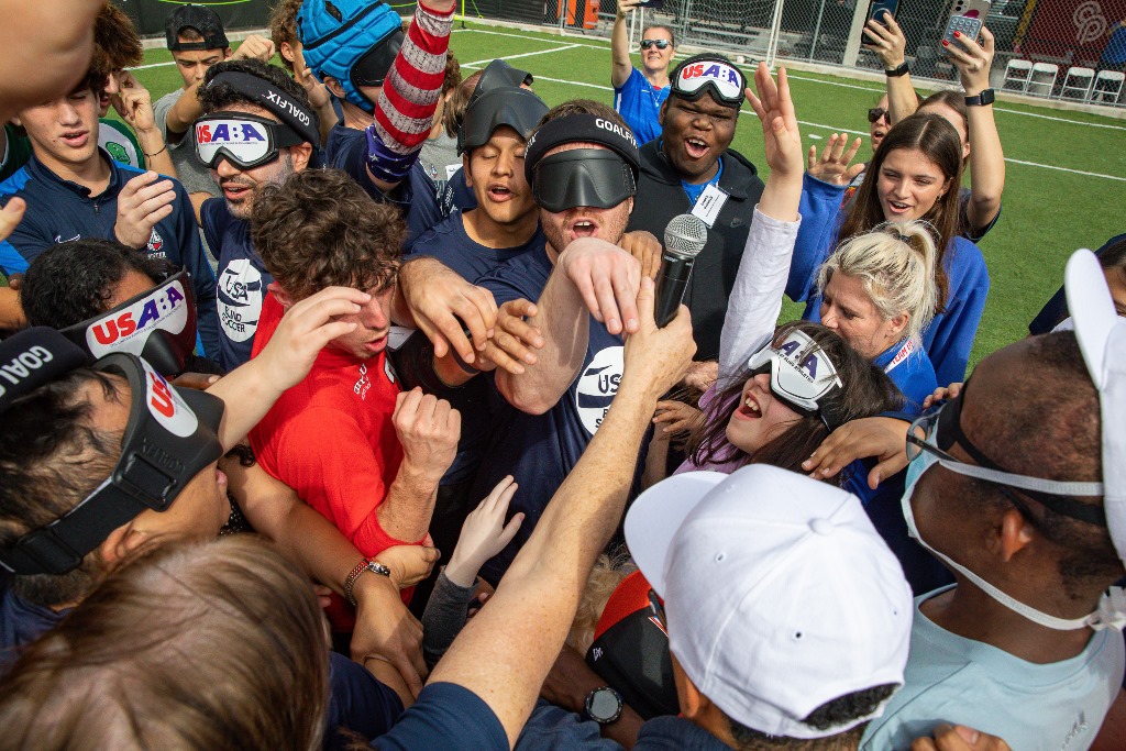 A group of participants and USA Blind Soccer athletes and coaches give a group cheer after a session