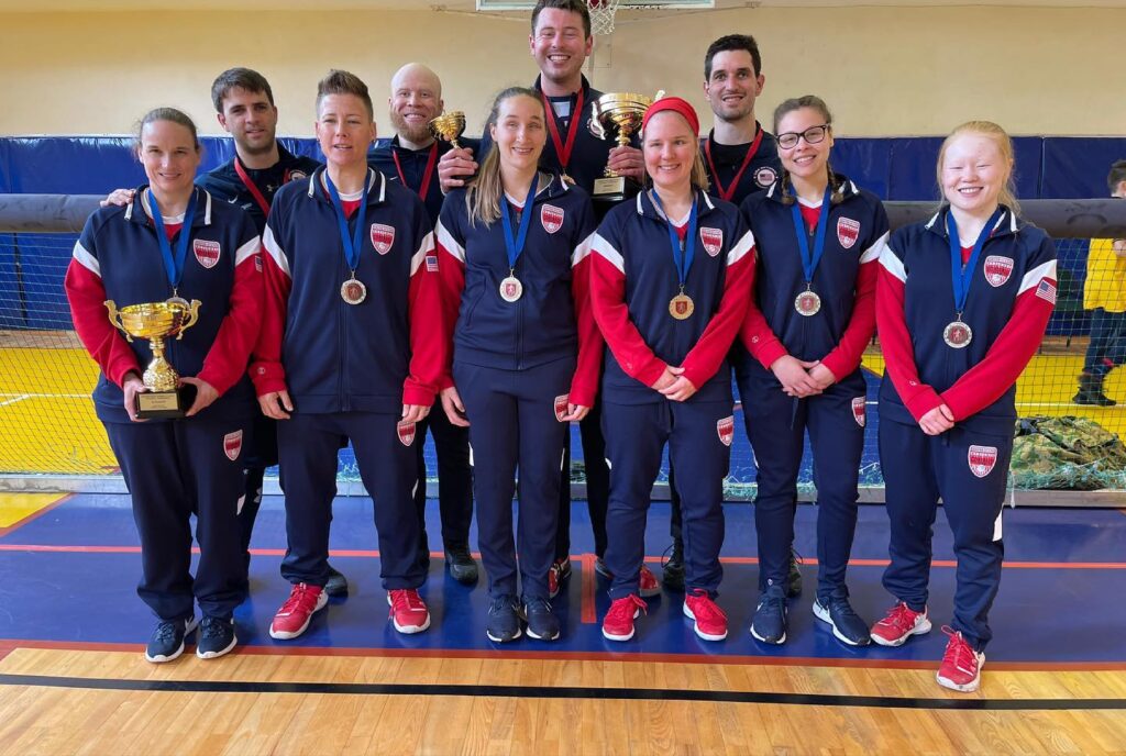 The USA Men's and Women's Goalball Teams pose on the court wearing their medals and holding trophies.